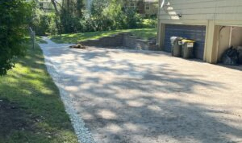 driveway pavement leading up to a house with a side brick wall running tangent to the side