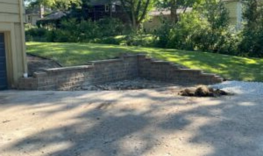 driveway pavement leading up to a house with a side brick wall running tangent to the side