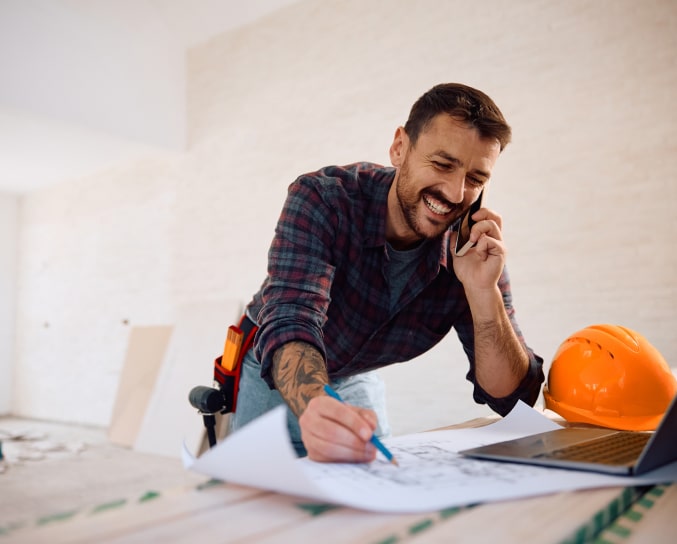 Construction worker writing on some plans while laughing on the phone